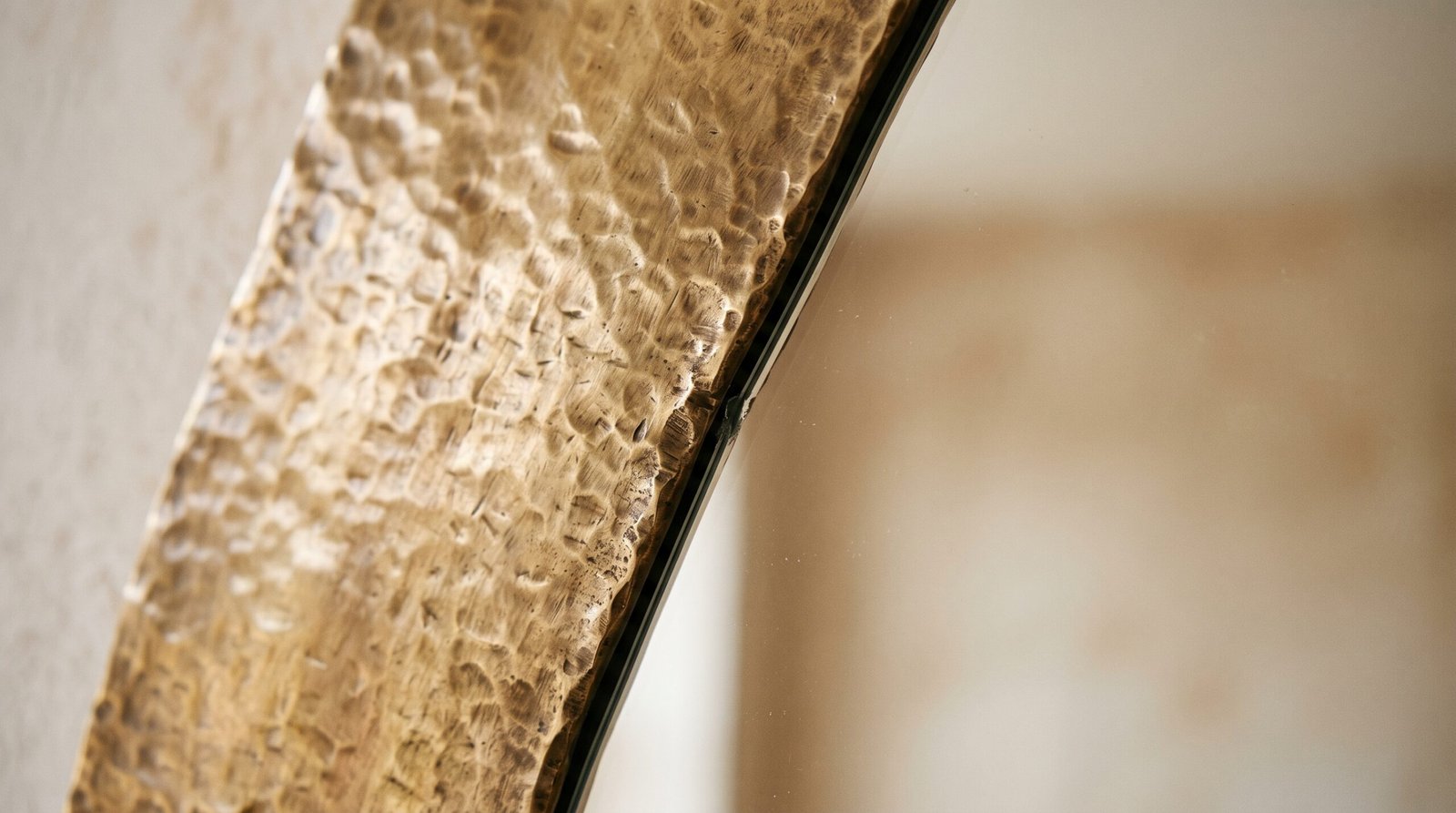 Close view of the edge of an unlacquered brass mirror frame where the metal meets the glass