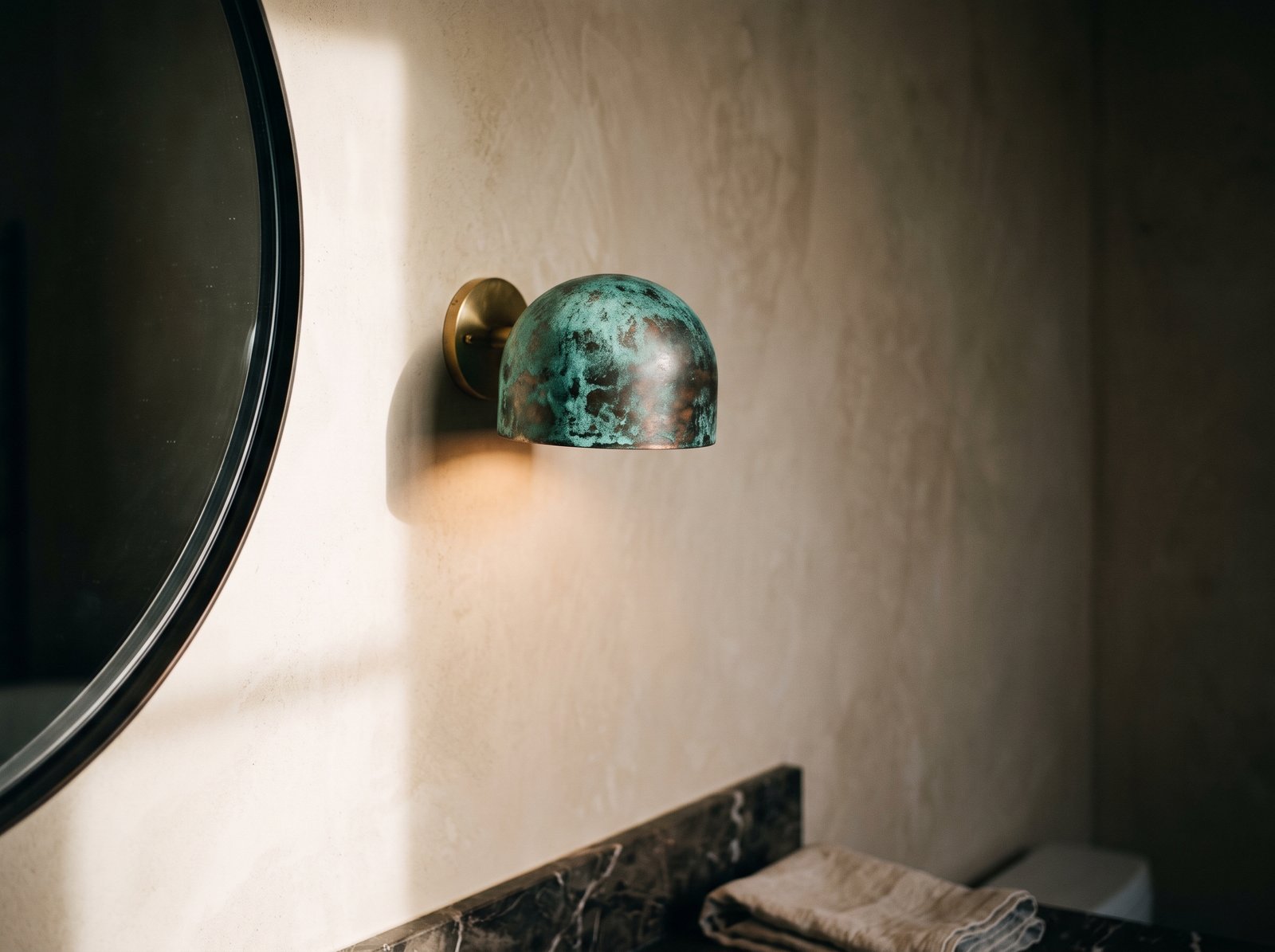 Verdigris copper dome wall sconce angled down on a plaster bathroom wall