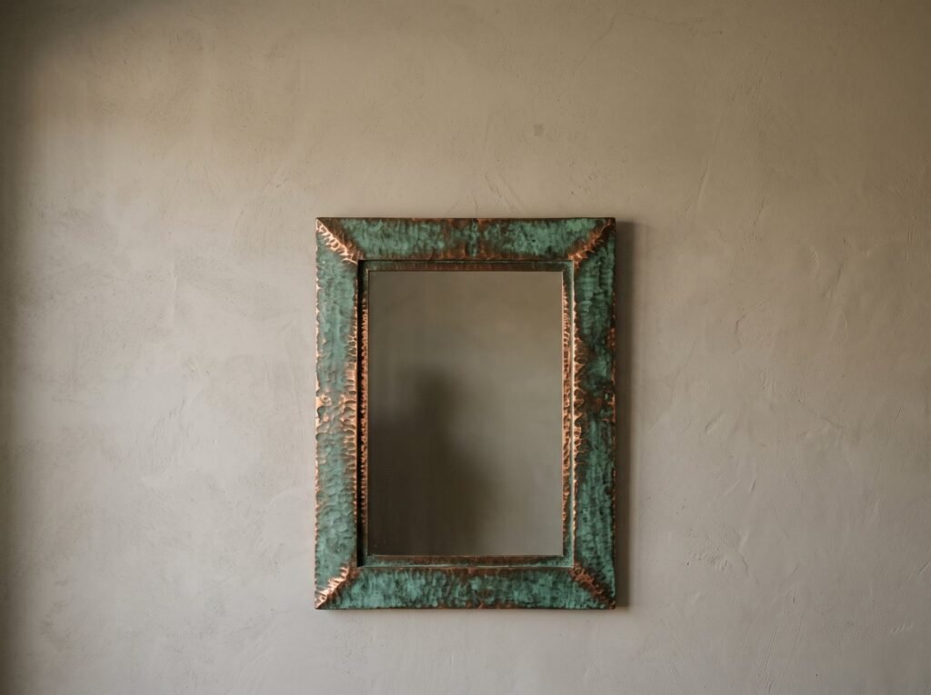 Rectangular copper mirror with a green verdigris frame on a plaster wall