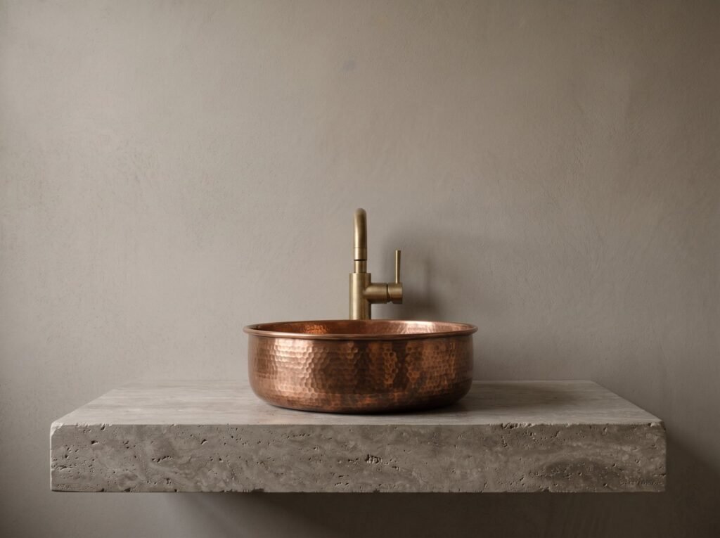 Round copper vessel sink with an unlacquered brass basin tap on a travertine vanity